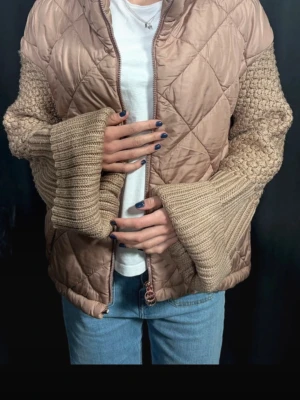 Beige quiltad jacka med stickade ärmar - Unik beige jacka med quiltat tyg på kroppen och breda, stickade ärmar i matchande ton. Dragkedja framtill och två fickor med dragkedja. Jackan är ifrån ett ur företag och säljs inte längre ❤️