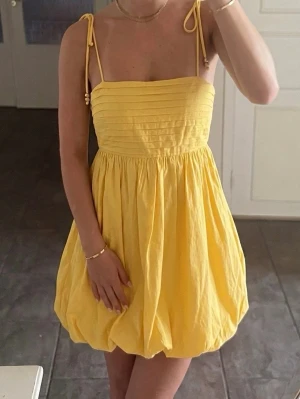 Gul söt Lipsy London klänning med smock i ryggen, Y2K / Boho storlek 38 - Superfin gul sommarklänning från Lipsy London i jättesöt ballongmodell i 100% bomull!💛 ✨  Klänningen har en jättefin passform med stretchig smock/resår i ryggen som gör att den sitter stadigt och bekvämt. Axelbanden är tunna, knytbara och har jättefina små pärlor i ändarna.   Modellen är helt rak framtill över bysten och går ut i en söt, fluffig babydoll-form nertill. Storlek 38 men passar även på mig som vanligtvis är en S pga smocken i ryggen.  Perfekt till midsommar, sommarfester & studenten!