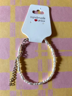Handgjort pärlarmband i vitt - Snyggt handgjort armband med vita pärlor i olika former och storlekar. Armbandet har en justerbar silverfärgad kedja för perfekt passform. Perfekt accessoar för att lyfta din stil.