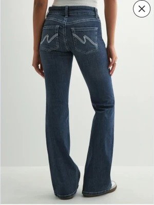 Bootcut jeans med kontrastsömmar - Mörkblå bootcut jeans med vita kontrastsömmar och dubbla knappar i midjan. Snygga fickor bak med zigzag-detaljer och klassisk femficksmodell. Jeansen har en lätt utsvängd passform och är perfekta för en avslappnad men trendig look.