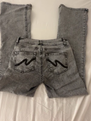 Grå bootcut jeans med broderade fickor - Säljer ett par grå jeans från NELLY som är lågmidjade och bootcut. Jeansen är lite skadade vid hälarna då de är lite långa för mig. Nya:ca 600kr, 350kr nu