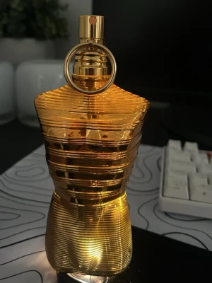 Jean Paul Gaultier Le Male Elixir absolu  - Exklusiv parfym i en guldig, kroppformad flaska från Jean Paul Gaultier. Flaskan har en metallisk finish och levereras med en röd sammetsbas och tillhörande guldfärgat fodral. Perfekt för dig som gillar lyxiga och unika dofter.