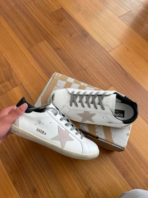 Vita Golden Goose strl 43/ helt nya - 👟 Märke: Golden Goose 📏 Storlek: 43 🎨 Färg: Vit med grå detaljer & klassisk stjärna ✨  🔥 Stilrena och exklusiva sneakers från Golden Goose – perfekta för både vardag och en clean streetwear-look. Den ikoniska designen med vintage-känsla gör att skorna passar till allt från jeans till shorts.  ✨ Skick: Helt nya, aldrig använda 📦 Kommer med originalkartong 🧼 Fräscha och redo att användas 👌 Perfekta för både vardag, resa och sommarfits