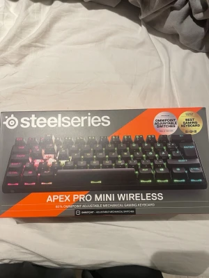 SteelSeries Apex Pro Mini Wireless - Trådlöst mekaniskt gamingtangentbord från SteelSeries, modell Apex Pro Mini Wireless. Kompakt 60% layout, svarta tangenter och RGB-belysning. Utrustad med Omnipoint justerbara mekaniska switchar och USB-C kabel. Perfekt för gaming och smidig att ta med.
