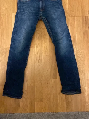 Mörkblå jeans från Tommy Jeans - Snygga mörkblå jeans från Tommy Jeans med klassisk femficksdesign och diskret logga på bakfickan. Jeansen har raka ben och är tillverkade i denim med lätt tvättad effekt för en cool look.