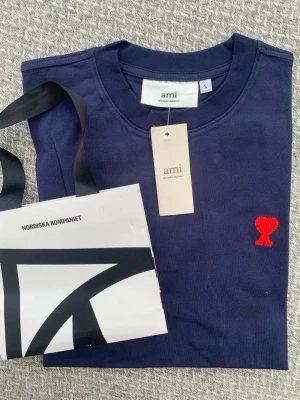 Mörkblå t-shirt från Ami Paris - Snygg mörkblå t-shirt från Ami Paris med klassisk passform och rund hals. T-shirten har Ami:s ikoniska röda hjärta broderat på bröstet. Tillverkad i mjuk bomull, perfekt för en stilren och trendig look.