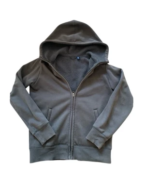 Grå uniqlo hoodie med dragkedja - Mysig grå hoodie med dragkedja och huva. Insidan är fodrad med mjukt teddyfoder som gör den extra varm. Två fickor framtill och ribbade muddar vid ärmslut och nederkant. Perfekt för kyliga dagar och chill outfits.