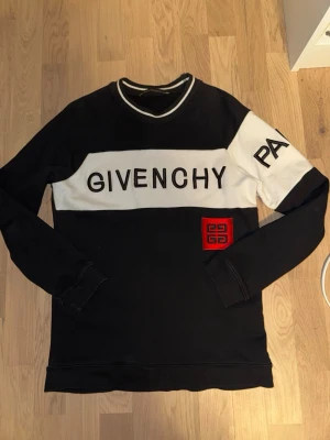 Svart och vit långärmad topp Givenchyy - Svart och vit långärmad topp från Givenchyy med stor logga framtill och röd broderad detalj. Kontrastfärgade partier och rund halsringning med vit kant. Snygg och trendig design som sticker ut.