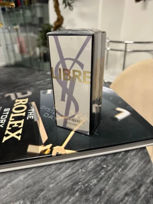 Yves Saint Laurent Libre EdP - Yves Saint Laurent Libre Eau de Parfum i elegant rektangulär flaska med guld- och silverdetaljer. Förpackningen har en lyxig design med stora YSL-bokstäver och LIBRE i guld. Perfekt för dig som gillar exklusiva dofter och snygg design.