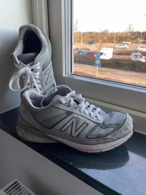 Grå New Balance sneakers - Klassiska grå New Balance sneakers med vit sula och vita skosnören. Skorna har meshpaneler för extra andningsförmåga och detaljer i mocka och syntet. Den ikoniska N-loggan syns tydligt på sidan. Perfekta för en sportig och avslappnad stil. Skorna är välanvända och behöver lite kärlek för att poleras upp, men de har definitivt mer att ge. Se bilder för skick, vad du ser är vad du köper.