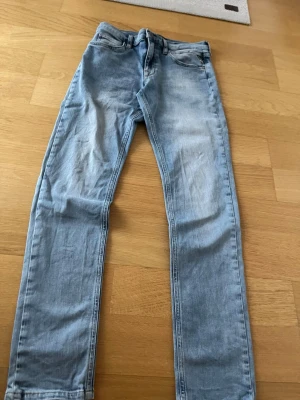 Ljusblå jeans från Replay - Säljer ett par ljusblå jeans från Replay med klassisk femficksmodell och snygga slitningar. Jeansen har raka ben och detaljerade bakfickor med broderi samt Replay-lapp i läder bak i midjan. Perfekta för en avslappnad och trendig look.