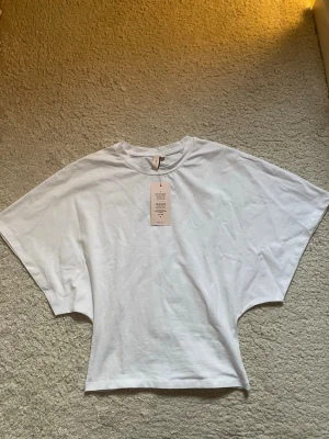 Vit oversized t-shirt från Nelly - Säljer en vit t-shirt från Nelly med rund hals och extra vida, korta ärmar. Tillverkad i mjuk bomull som känns skön mot huden. Ny med prislapp kvar!!