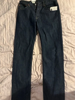 Mörkblå raka jeans från Levi's - Säljer ett par mörkblå raka jeans från Levi's med klassisk femficksdesign och knappgylf. Jeansen har en tidlös look och är tillverkade i slitstark denim. Perfekta för dig som gillar en clean och enkel stil.