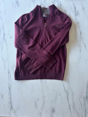 Vinröd halvzip-tröja från Morris - Vinröd stickad tröja från Morris med halv dragkedja och diskret logga på bröstet. Tröjan har ribbade muddar och är tillverkad i merinoull. Perfekt för lager-på-lager och snygg till jeans. Mycket bra skick nästa nytt. Använd få tal gånger.