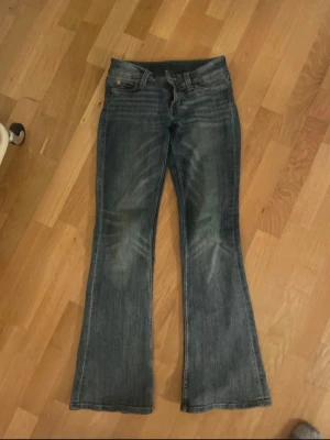Blå bootcut Jeans - Ett par blå bootcut jeans med snygga slitningar och lätt tvättade detaljer på låren. Jeansen har klassisk femficksdesign och normal midja. Perfekta för dig som gillar en avslappnad och trendig look. Storlek 24/30