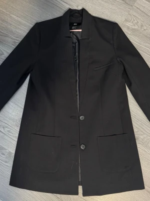 Svart kavaj från H&M med fickor - Stilren svart kavaj från H&M med två knappar framtill, två stora fickor och en bröstficka. Kavajen har rak passform 