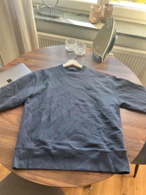 Mörkblå sweatshirt från Acne Studios - Snygg mörkblå sweatshirt från Acne Studios med klassisk rund hals och deras ikoniska face-logga på bröstet. Tröjan är i mjukt bomullsmaterial och har en avslappnad passform. Perfekt för en stilren och enkel look. Tröjan är perfekt och snygg, andvänd 2 gånger😄🤩