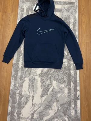 Mörkblå Nike hoodie med byxa till - Snygg mörkblå hoodie från Nike med klassisk ljusblå swoosh-logga på bröstet. Hoodien har huva, lång ärm och en stor känguruficka framtill. Perfekt för en avslappnad och sportig stil. Tillverkad i mjukt material för extra komfort. Därmed kommer byxorna till hoodien alltså att jag säljer en nike set. Finns tagg o så på byxan men på tröjan har jag råkat ta av o sedan slängt. Nike setet är nytt alltså har jag bara testat setet o tyvärr passade den ej.