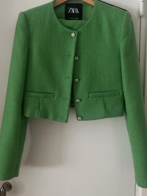 Grönt set från Zara med kavaj och shorts - Snyggt grönt set från Zara med kort kavaj och matchande shorts i strukturerat tyg. Kavajen har dekorativa knappar med stenar och två fickor framtill. 💕🩷