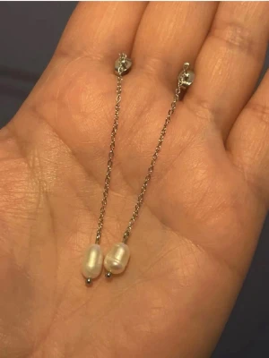 kedjeörhängen liknar Edblad modell perla - Säljer ett par stilrena silverfärgade örhängen med tunn kedja och minimalistisk design. Örhängena har små pärlliknande detaljer vid fästet och passar perfekt för dig som gillar diskreta accessoarer.