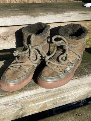 Inuikii Boots - Säljer ett par skor från INUIKII i färgen oliv, med mjukt ullfoder och grova snören som går kors och tvärs över skon. Yttermaterialet är mocka och sulan är i gummi. Använda sparsamt en säsong. Perfekta för kalla dagar när du vill hålla stilen och värmen. Liten i stl, tänk att du behöver en stl större än du brukar ha. 