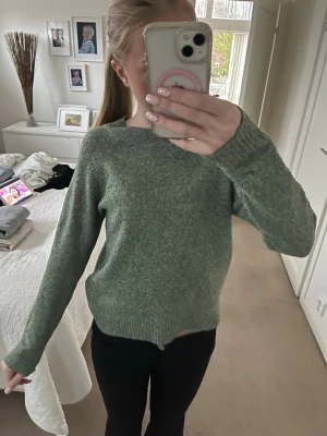Grön stickad tröja med rund hals - Mysig stickad tröja i en dämpad grön nyans med rund hals och långa ärmar. Tröjan har ribbstickade muddar vid ärmslut och nederkant, vilket ger en snygg och enkel look. Perfekt att matcha med jeans eller leggings.