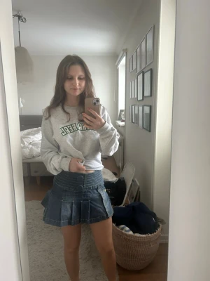 Blå mini jeanskjol med volang - Säljer en blå kort jeanskjol med volangdetaljer och bred linning. Kjolen har en klassisk denimlook och är perfekt för dig som gillar en trendig och ungdomlig y2k-stil. Passformen är normal och materialet är bomull. Inga synliga mönster eller loggor.