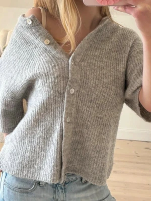 Gina kofta - Mysig grå ribbstickad kofta med kort ärm och knäppning framtill. Koftan har en avslappnad passform och är perfekt att slänga över en topp. Enkel och stilren design som funkar till det mesta.