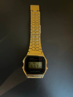 Guldig digital klocka från Casio - Stilren digital klocka från Casio i guldigt rostfritt stål. Klassisk rektangulär urtavla med digital display och länkarmband. Perfekt accessoar för dig som gillar retrostil och enkelhet.
