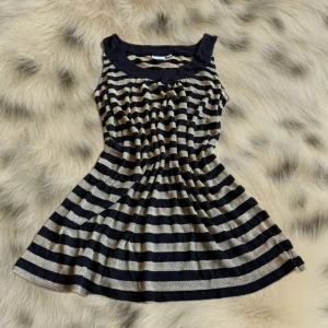 Randig topp från Glamorous - Säljer en lång, ärmlös topp från Glamorous med svarta och guldiga horisontella ränder. Den  har en bred, svart kant vid ringningen och ett lätt utställd passform.