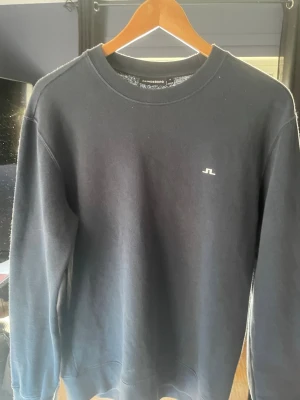 sweatshirt från J.Lindeberg - Klassisk svart sweatshirt från J.Lindeberg med rund halsringning och diskret logga på bröstet. Tröjan har ribbade muddar vid ärmslut och nederkant, perfekt för en clean och stilren look. Tillverkad i mjukt bomullsmaterial.