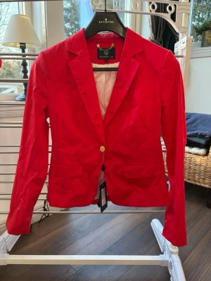 Röd kavaj från Stockh LM - Snygg röd kavaj från Stockh LM med klassisk krage. Helt oanvänd, prislappen finns kvar. Köparen står för frakt 