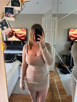 Beige ribbad stickad kortklänning - Mysig beige stickad klänning med ribbad struktur och lång ärm. Klänningen är kort och har en djup v-ringning som ger en trendig look. Perfekt för dig som gillar en enkel men snygg stil.