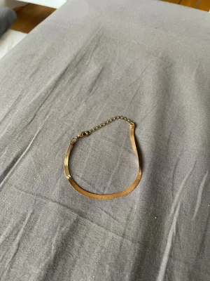 Guldigt platt armband med kedja - Snyggt armband i guldton med platt, slät design och justerbar kedja. Perfekt för dig som gillar stilrena accessoarer med en modern touch. Armbandet har ett klassiskt spänne och passar till många olika looks.