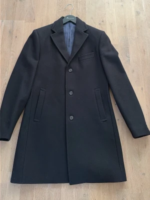 Snygg svart från Morris - Klassisk svart rock från Morris i ull med tre knappar framtill, två snedställda fickor och en bröstficka. Rocken har slät fodrad insida och stilren design med krage och slag. Perfekt för dig som vill ha en tidlös och elegant look.