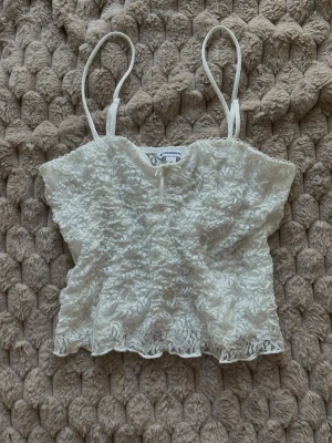 Vitt spetslinne - Clockhouse  - Superfint vitt spetslinne från Clockhouse. Ryggen är genomskinlig spets, medans framtill är det extra tyg. Det är en gullig rosett framtill, och smala axelband. Storlek S, men passar mer som XS. Oanvänt.