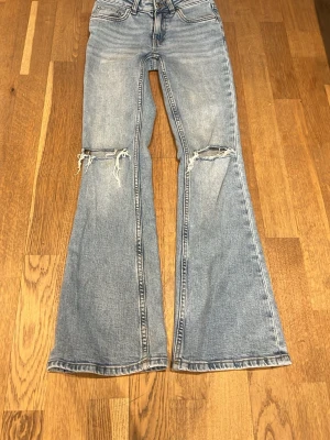 Bootcut jeans från 157 - Ljusblå bootcut jeans från 157 med låg midja och slitna detaljer över knäna. Jeansen har klassisk femficksdesign och är tillverkade i denim. Perfekta för dig som gillar en avslappnad och trendig look.
