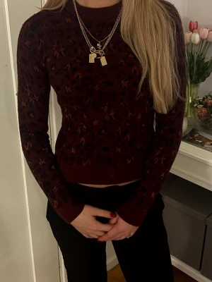 Vinröd leopardmönstrad stickad tröja från & Other Stories - Snygg vinröd stickad tröja med svart och mörkrött leopardmönster. Tröjan har rund halsringning, långa ärmar och ribbade muddar vid ärmslut och nederkant. Perfekt för dig som vill ha en trendig och bekväm look. Obs! Tröjan är väldigt tajt och liten i storlek. 