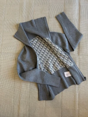 Grå kofta med mönster och dragkedja - Snygg grå kofta med dragkedja och ribbade muddar. Insidan har ett unikt vitt och grått mönster som ger extra stil. Perfekt för att hålla sig varm och se cool ut. Materialet känns mjukt och bekvämt, och koftan har hög krage.