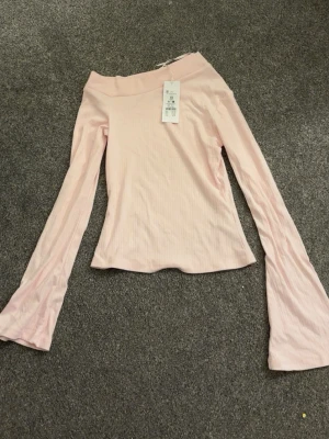 Ljusrosa one shoulder topp XS - Supersnygg ljusrosa one shoulder topp från Gina 14+  i ribbad bomull. Toppen har långa ärmar med lätt utsvängd form och sitter tight. Perfekt för dig som vill ha en trendig och stilren look.