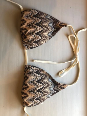 Mönstrad bikiniöverdel från BeckSöndergaard - Snygg trekantsbikini från BeckSöndergaard med brunt och beige mönster. Klassisk modell med knyt i nacke och rygg. Den är helt oanvänd och har inga defekter. 