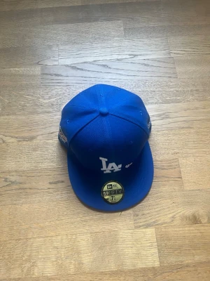 Blå LA Dodgers keps New Era - Snygg blå keps från New Era 59FIFTY med LA Dodgers-logga broderad framtill. Klassisk flat brim och broderade detaljer på sidorna. Tillverkad i ett slitstarkt material som känns sportigt och trendigt. Perfekt för dig som vill ha en ikonisk streetwear-look.