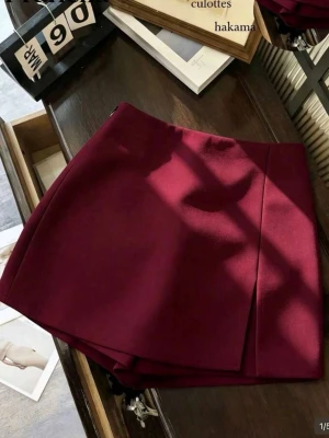 Vinröd skort med omlott-look - Trendig vinröd skort med snygg omlott-design framtill. Modellen har en rak passform och är tillverkad i ett slätt tyg som ger en stilren känsla. Shorts under kjolen, slit på sidan. Aldrig använd 