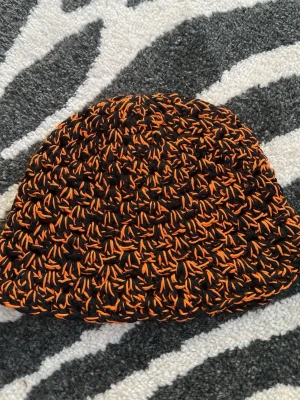 Handvirkad svart och orange mössa - Unik handvirkad mössa i svart och orange bomulls garn. Sitter bra på mig med 55cm i omkrets på huvudet