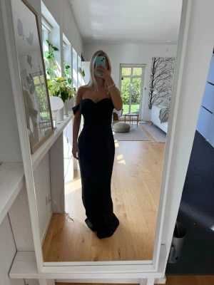 Svart långklänning med offshoulder - Elegant svart långklänning med offshoulder-design och figurnära passform. Klänningen har en hjärtformad urringning och markerad midja som ger en snygg siluett. 