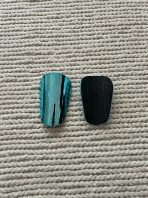 Blå metallic benskydd från skillsocks  - Blanka benskydd i metallicblå plast från  Skillsocks. Framsidan har en diskret logga och baksidan är svart med mönster för extra grepp. Ergonomisk form som passar bra vid sport och träning. Använda 2 träningar!