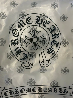 Vit Chrome Hearts t-shirt - Snygg vit t-shirt från Chrome Hearts med deras ikoniska logga och blommönster. T-shirten har klassisk passform och är perfekt för dig som gillar streetwear och exklusiva märken. Materialet är mjukt och bekvämt bomull.