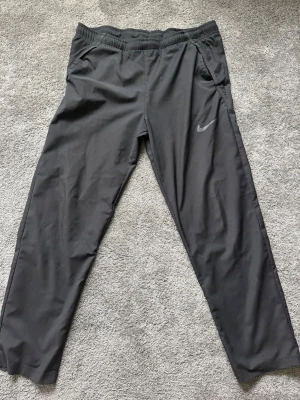 Svarta mjukisbyxor från Nike - Svarta mjukisbyxor från Nike med diskret logga på låret. Byxorna har resår i midjan och sidofickor. Tillverkade i ett mjukt och följsamt material som passar perfekt för en avslappnad stil.