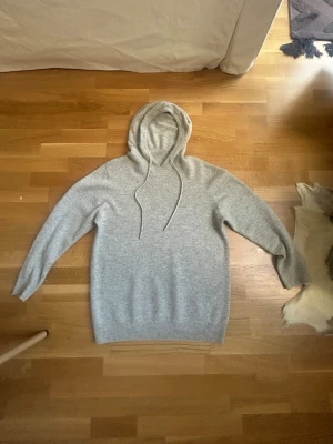 Ljusgrå merinoull hoodie - En stilren ljusgrå hoodie med huva och dragsnören. Hoodien har en enkel design utan tryck eller logga och är tillverkad i ett mjukt, stickat material. Perfekt för en avslappnad och bekväm look. Hoodien är köpt från Plick vilket är varför den inte har en lapp, köpte den för 649 i storlek M.