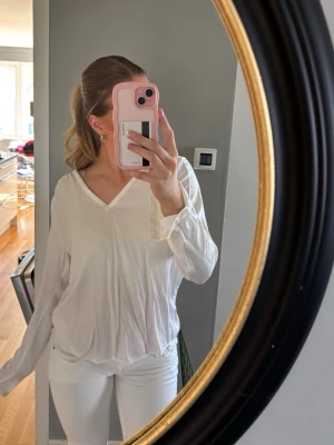 Vit v-ringad blus - Säljer en luftig vit blus med v-ringning och lång ärm. Blusen har en snygg spetsdetalj baktill och är tillverkad i ett lätt, mjukt tyg som ger en avslappnad look. Perfekt att styla med jeans eller kjol för en fräsch outfit. Har en jätteliten fläck som man ser på sista bilden.